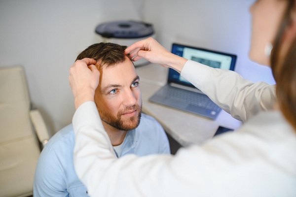 tricóloga examina en primera instancia, las pronunciadas entradas de cabello del paciente masculino