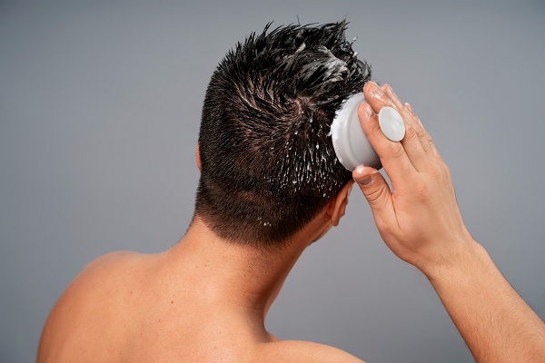 un hombre se realiza un masaje suave en el cuero cabelludo, con productos naturales, para cuidado del cabello